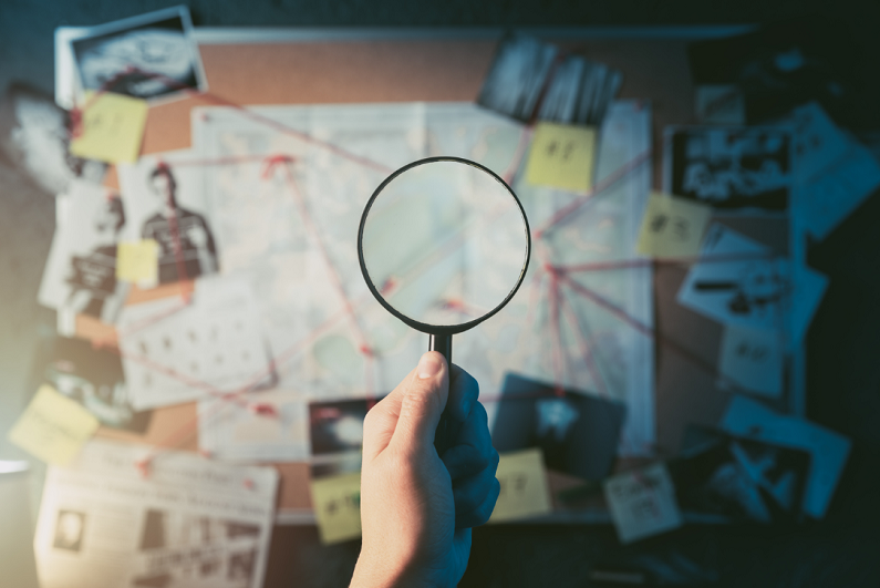 Detective hand holding a magnifying glass in front of a board with evidence.