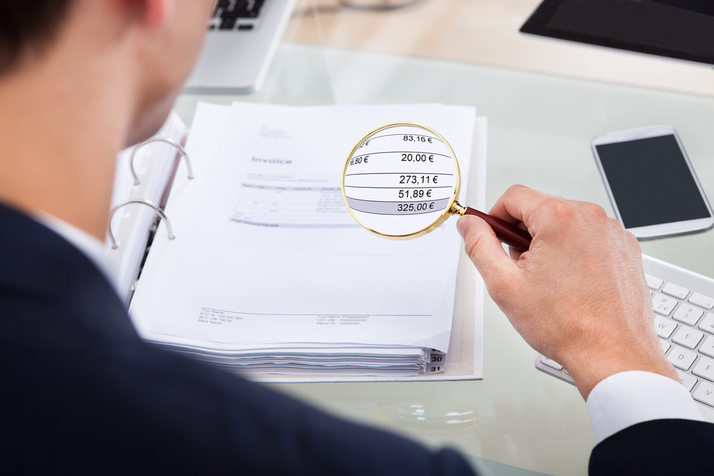 auditor examining invoice with magnifying glass at desk