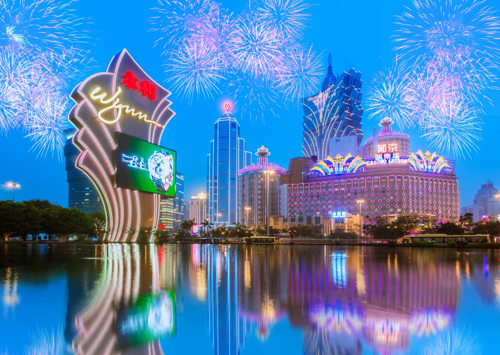 Illuminated Macau casinos stand against a fireworks-lit evening sky