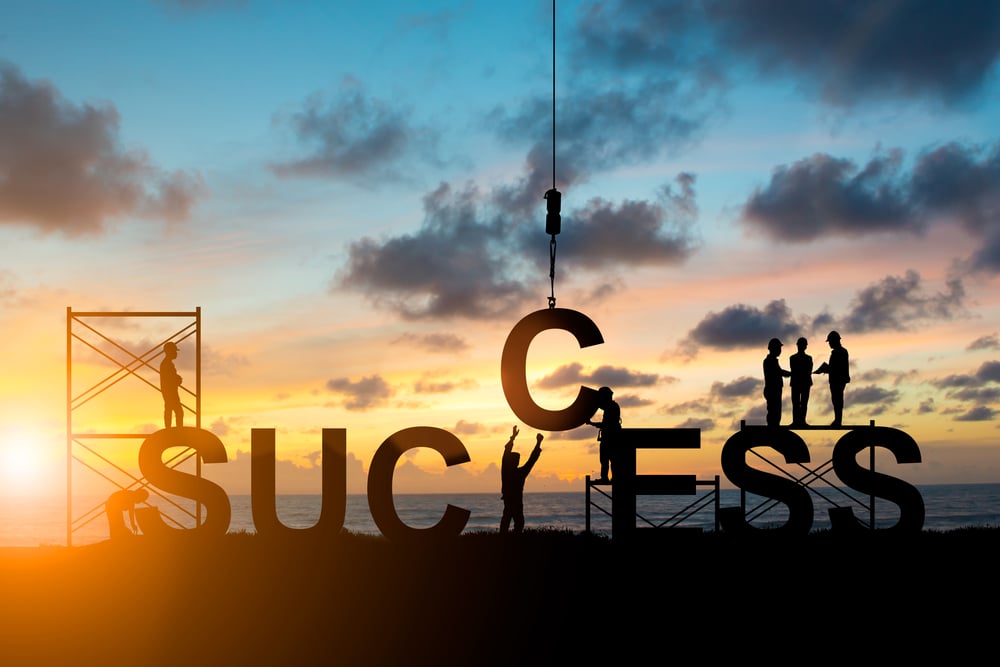 team of people constructing the word success against a sunset background