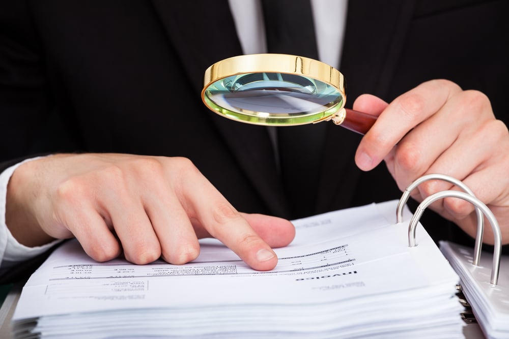 Businessperson holds magnifying glass while examining an invoices file