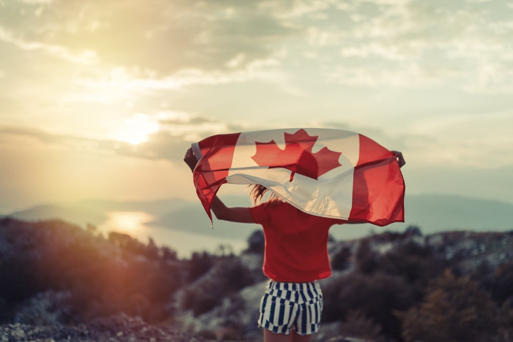 Female holds Canada flag while looking at the setting sun